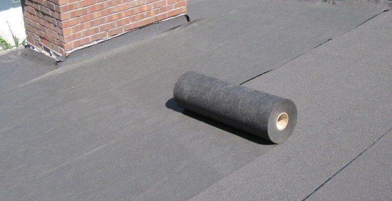 A black EPDM flat roof with a membrane roll and a brick chimney, repaired by GMG Roof Experts in the Hillingdon area