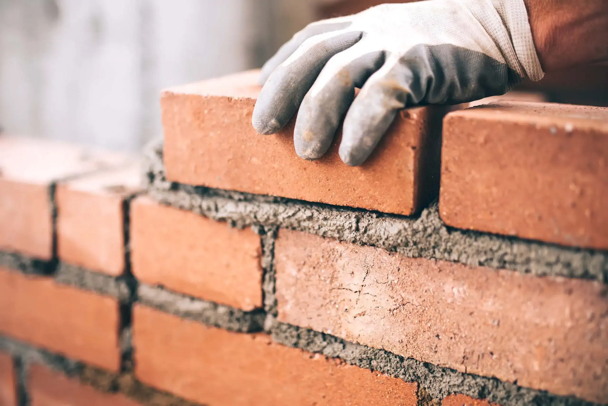 Bricklayer laying a brick onto a fresh mortar bed on a red brick wall, brickwork repairs by GMG Roof Experts across the London Borough of Hillingdon